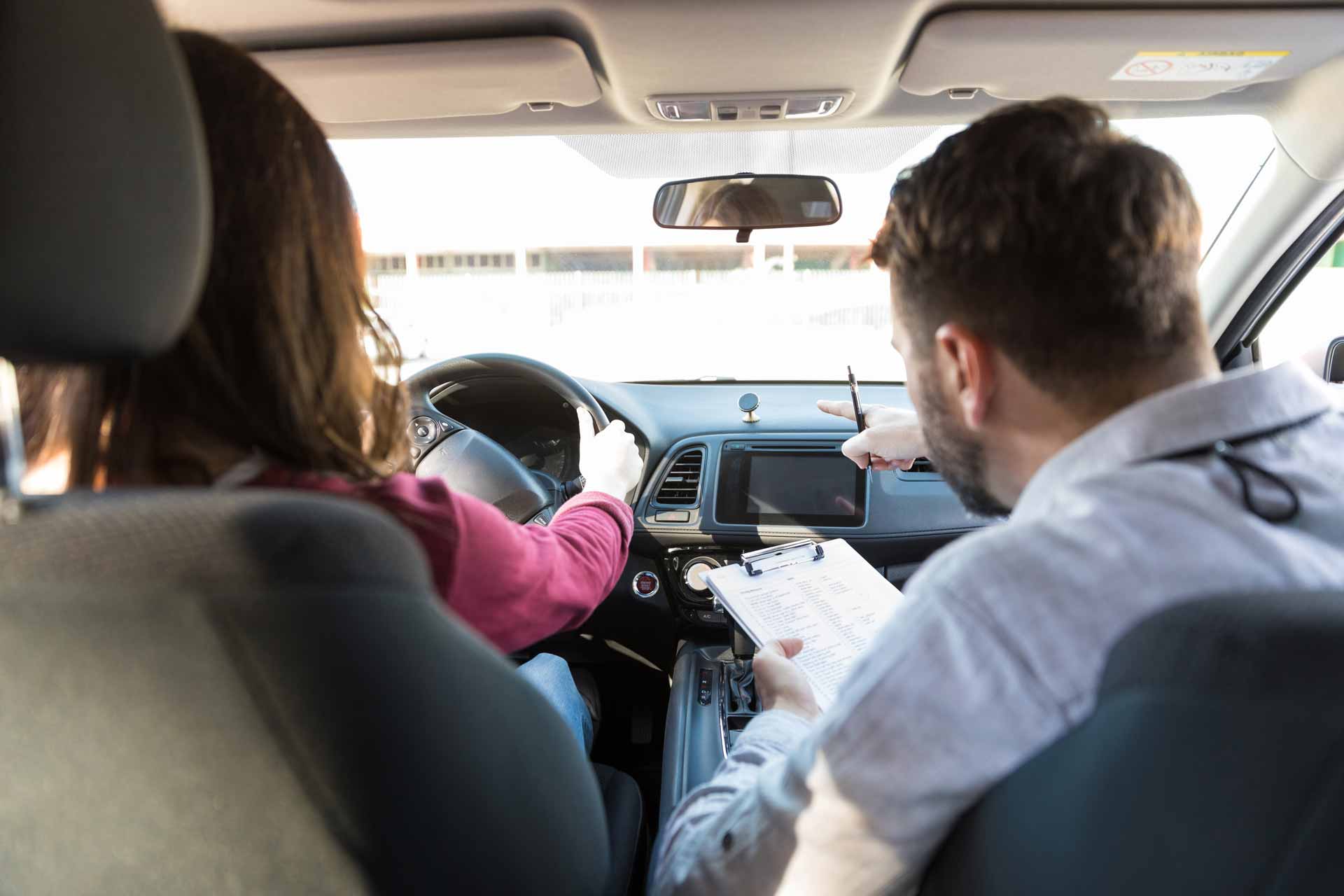 Adult student driving a car while an instructor points out the road ahead